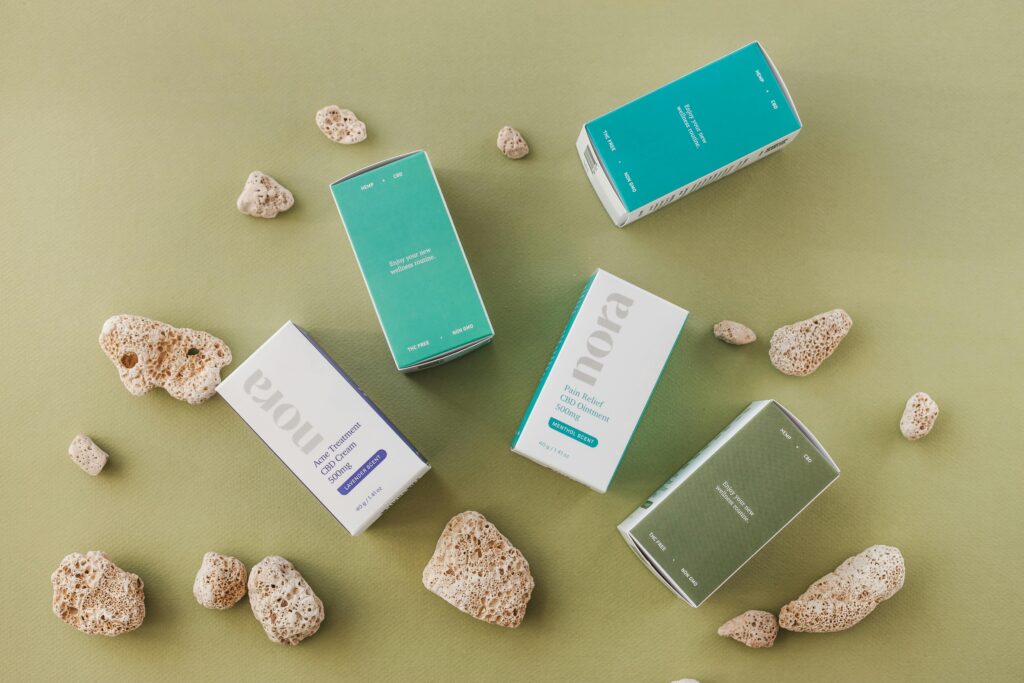 Top view of Nora CBD product packaging amidst rocks on a green surface.