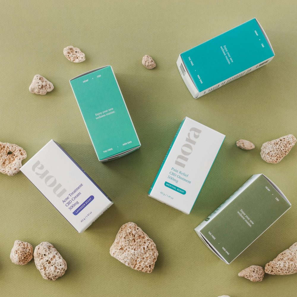Top view of Nora CBD product packaging amidst rocks on a green surface.